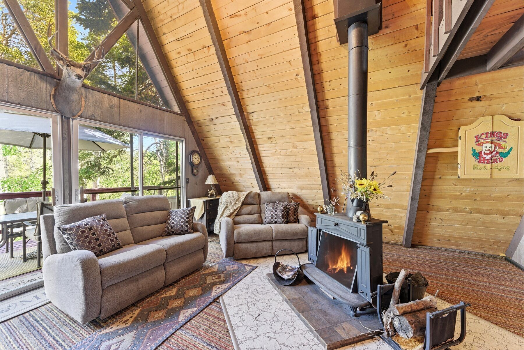 Timber Lakes cabin living room with wood stove, wood-paneled vaulted ceiling, and forest view