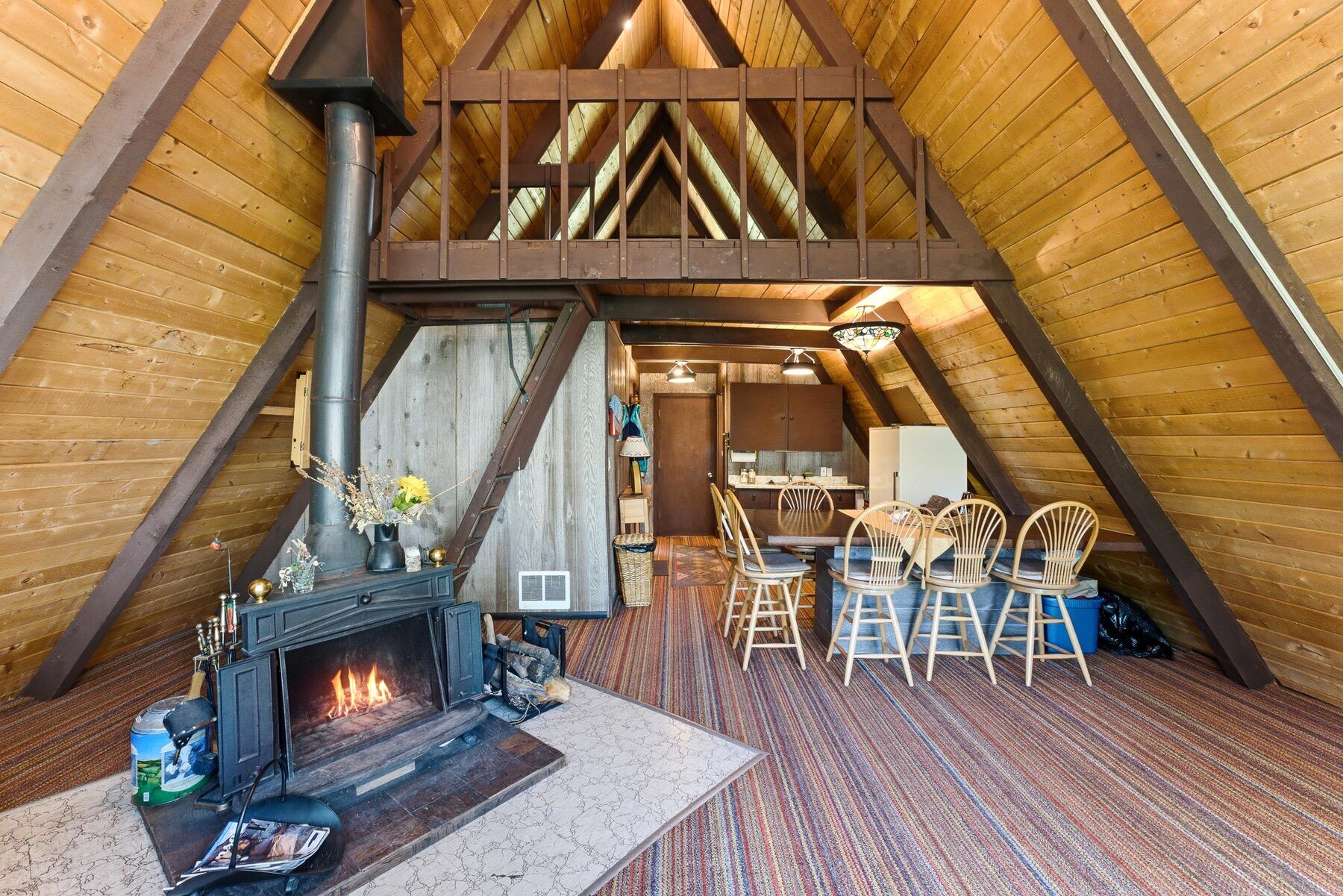 Warm A-frame great room with lit wood stove and dining area in Timber Lakes cabin